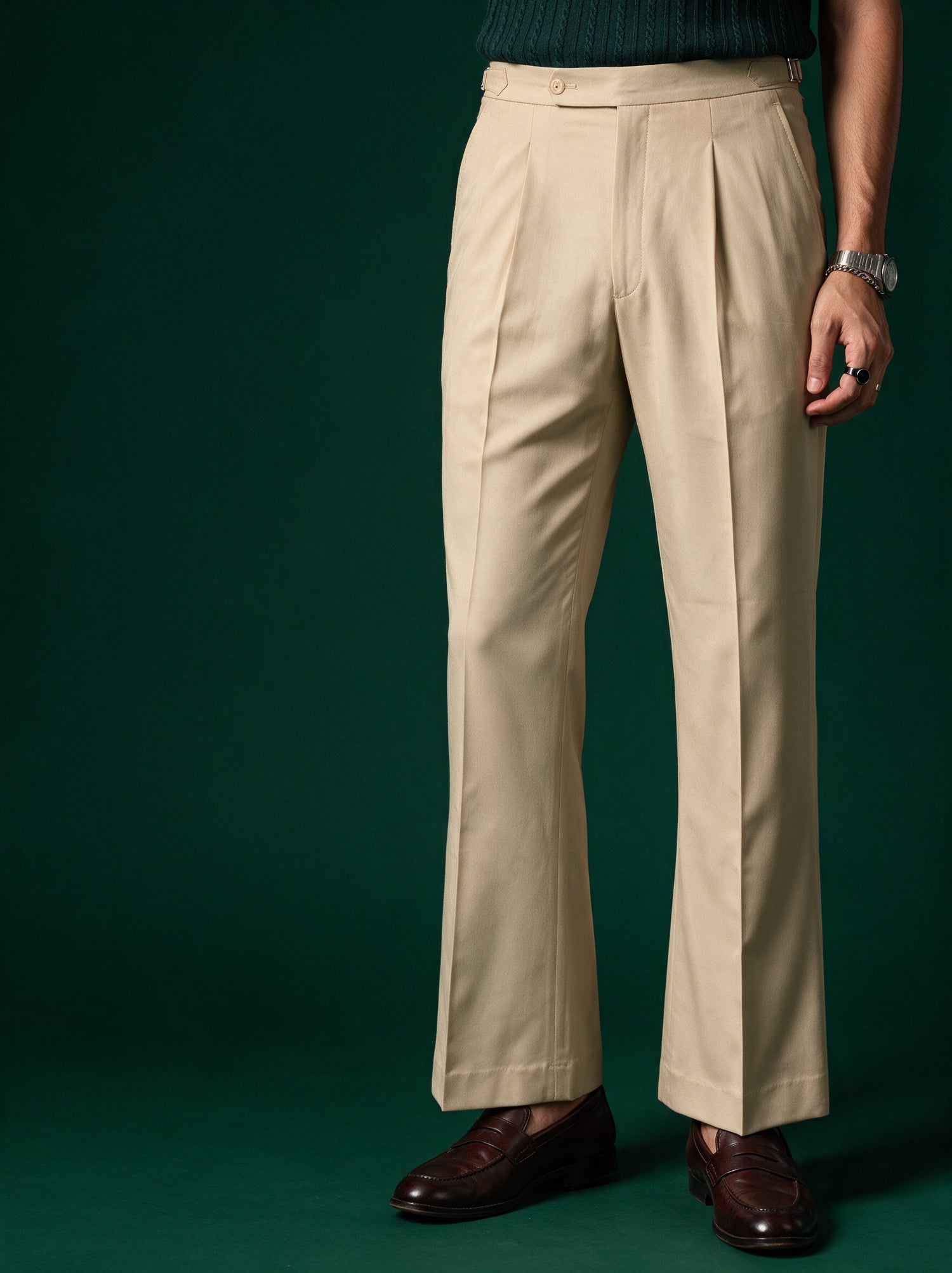 Cream double-pleated Drip Club tailored trousers with side adjusters and brown leather loafers against a deep green backdrop